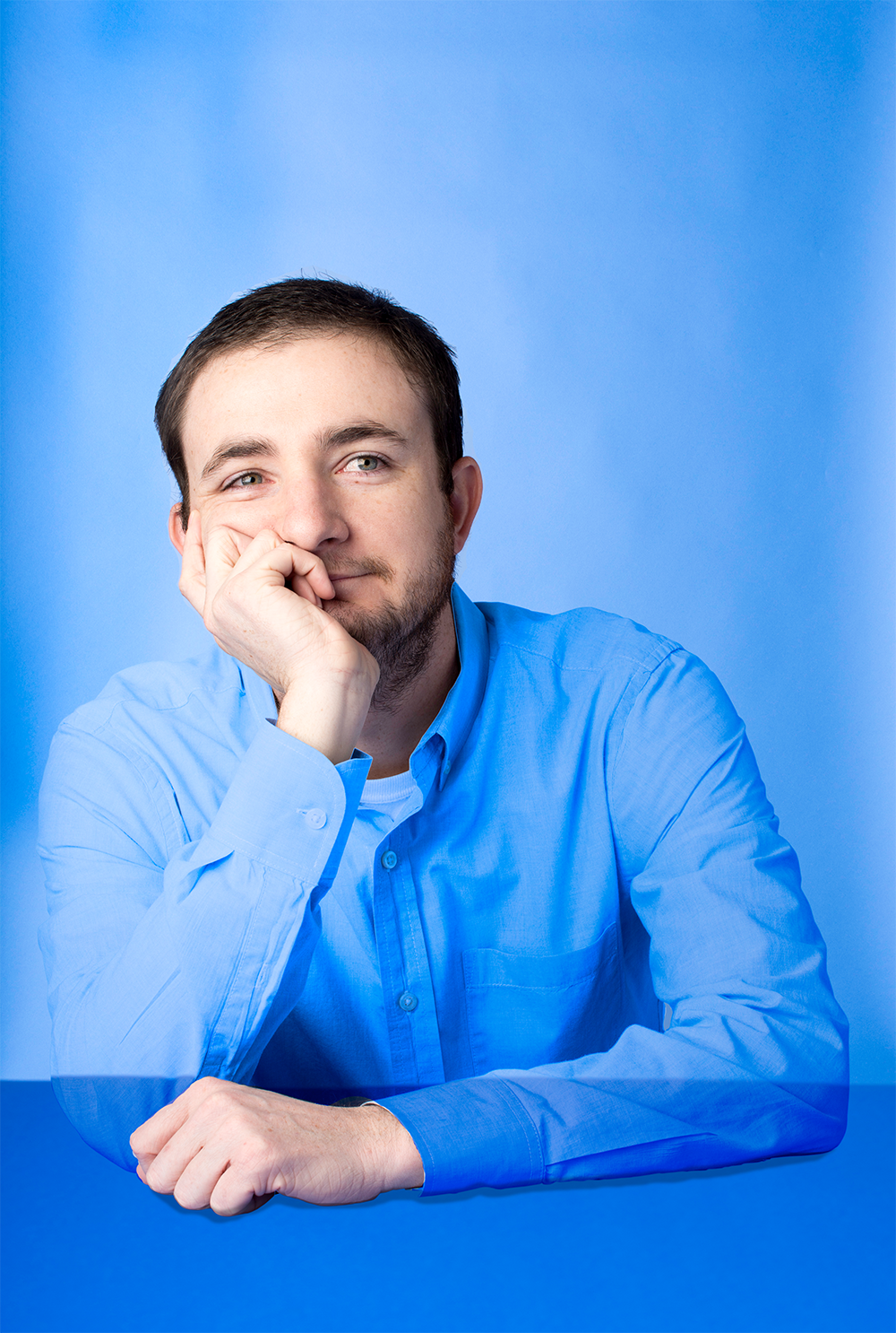 James McAlister, copywriter, leaning on his hand against a blue backdrop